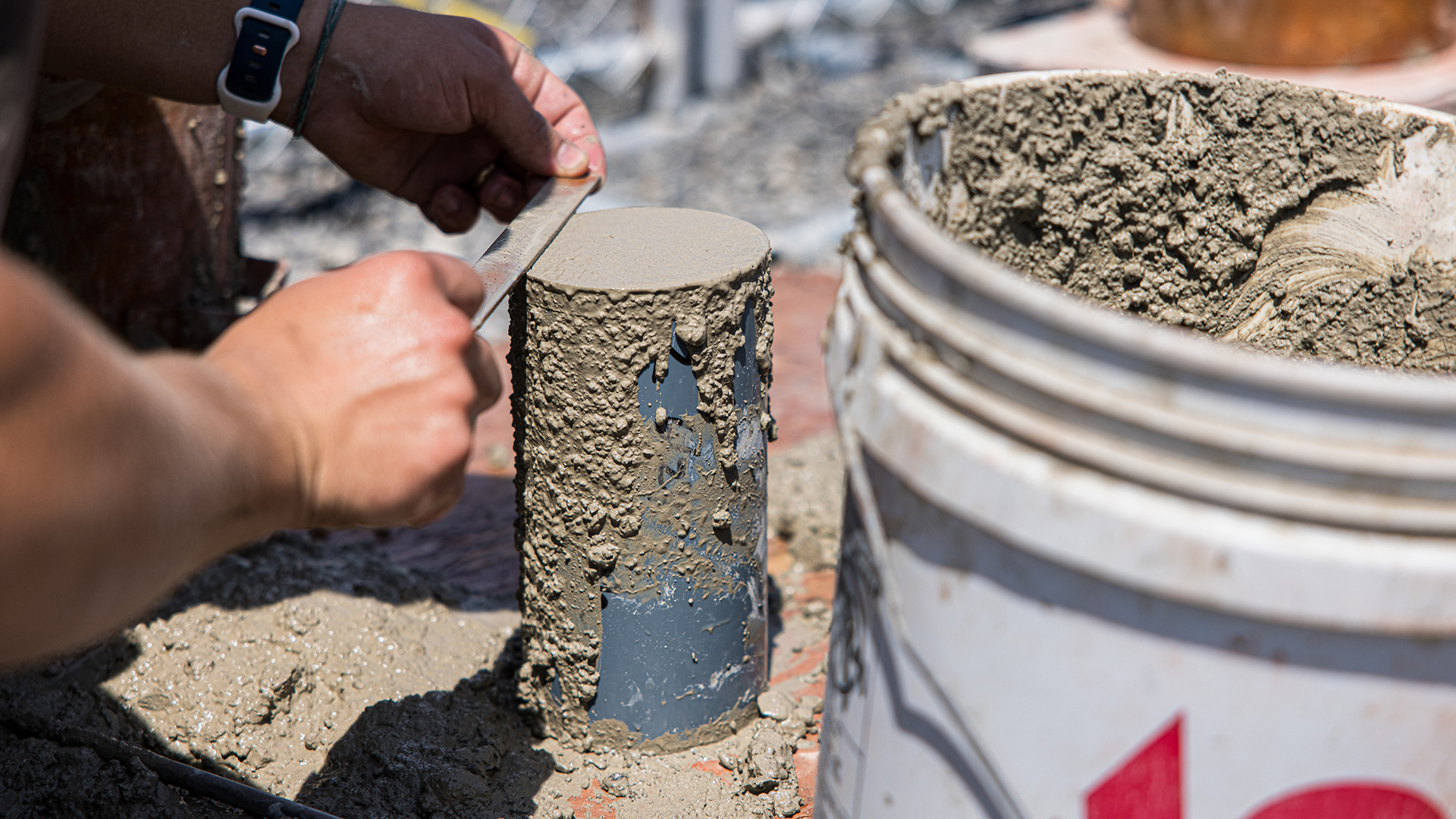 A worker uses a concrete smoother on top of a metal canister