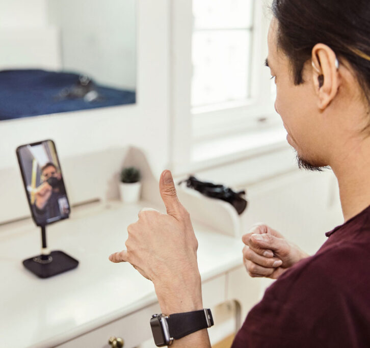 Man giving a thumbs up to another man whose image appears on a mobile phone