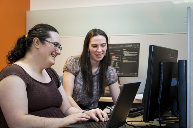 Female student works at a computer in university security operations center while woman looks on.