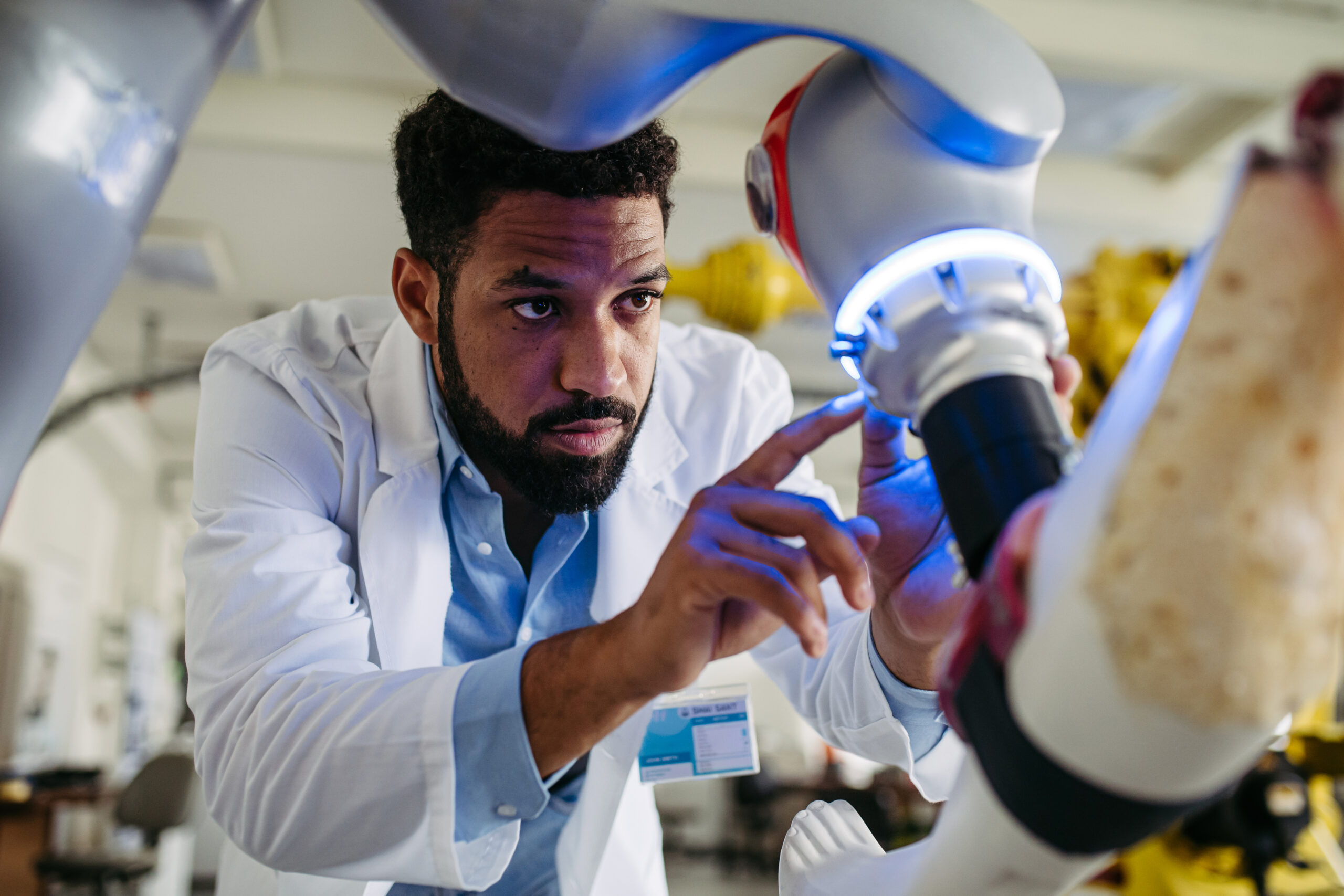 A scientist in a lab coat closely examines tech that has a glowing blue light.