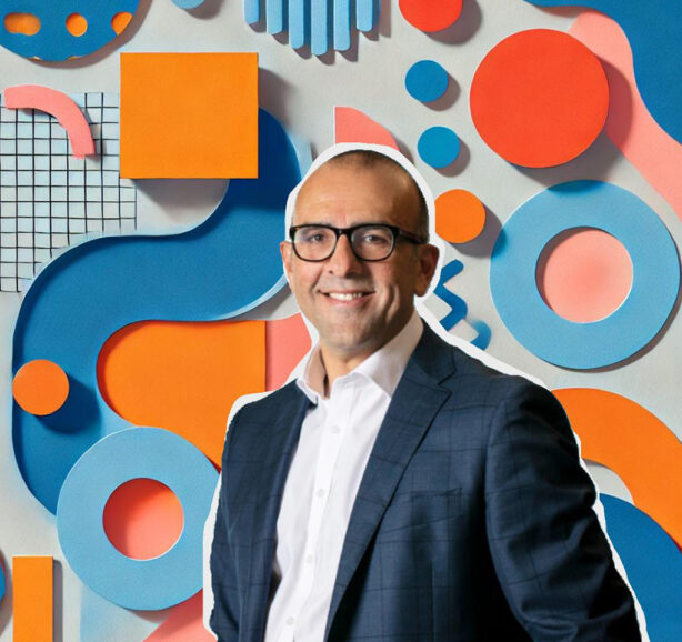 Man wearing glasses smiles as he looks forward, with a backdrop of colorful shapes.